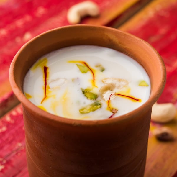 Indian lassi drink in a clay cup, garnished with saffron, pistachios, and cashews.