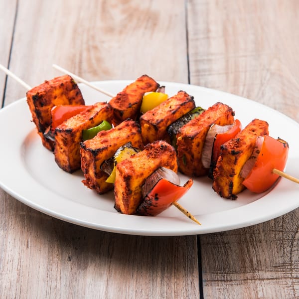 Tandoor Restaurant's paneer tikka skewers with red and green bell peppers and onions on a white plate.
