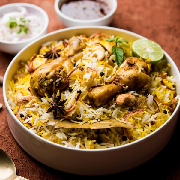 Chicken Biryani with rice, cashews, and spices, garnished with mint and lime, served with raita and chutney.
