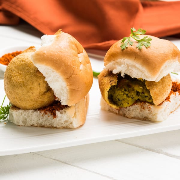 Two Indian vada pavs, one with a green filling, on a white plate with an orange napkin.