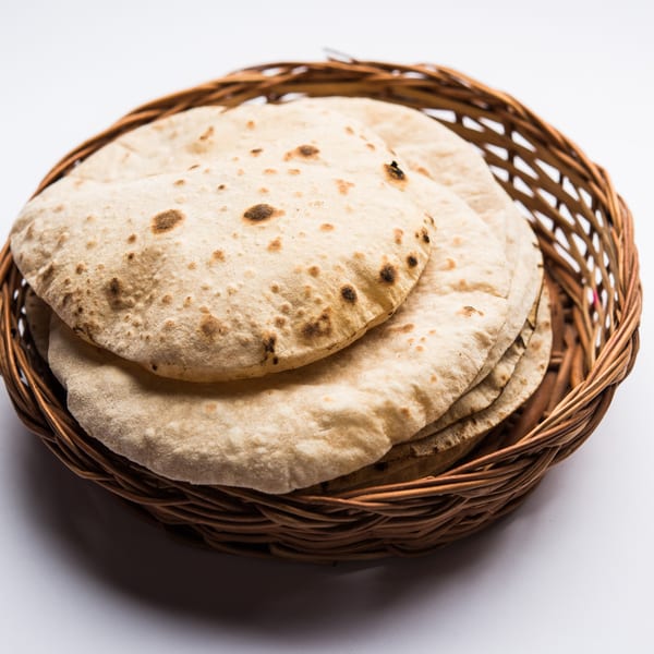 A woven basket filled with several pieces of freshly baked, round Indian flatbread (chapati).